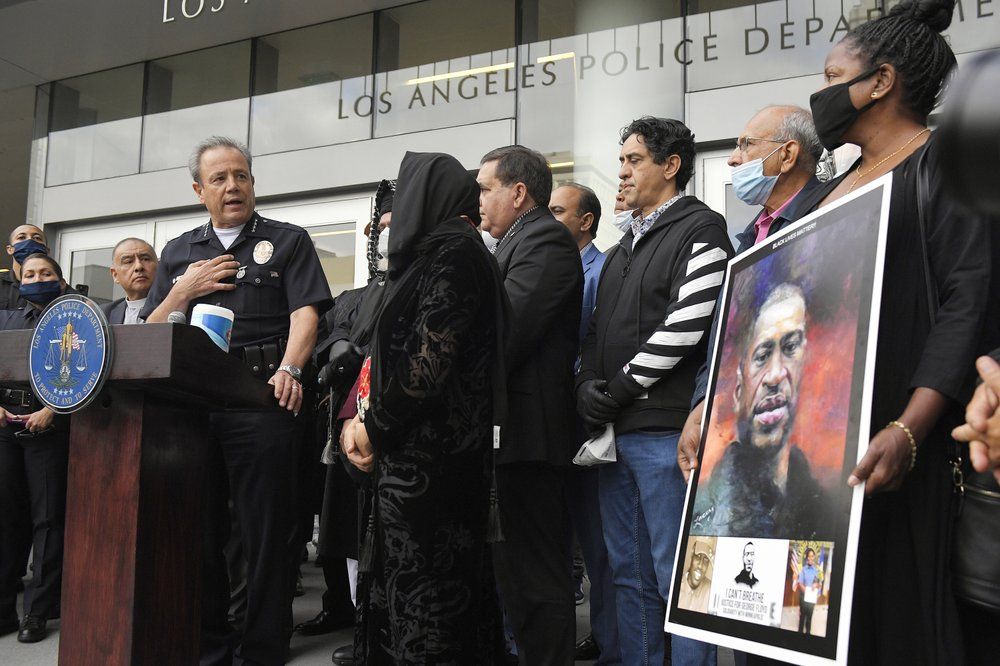 In this June 5, 2020, file photo, Los Angeles police chief Michel Moore, left, speaks as someone holds up a portrait of George Floyd during a vigil with members of professional associations and the interfaith community at Los Angeles Police Department headquarters in Los Angeles. The Los Angeles Police Department launched an internal investigation after an officer reported that a photo of Floyd with the words 