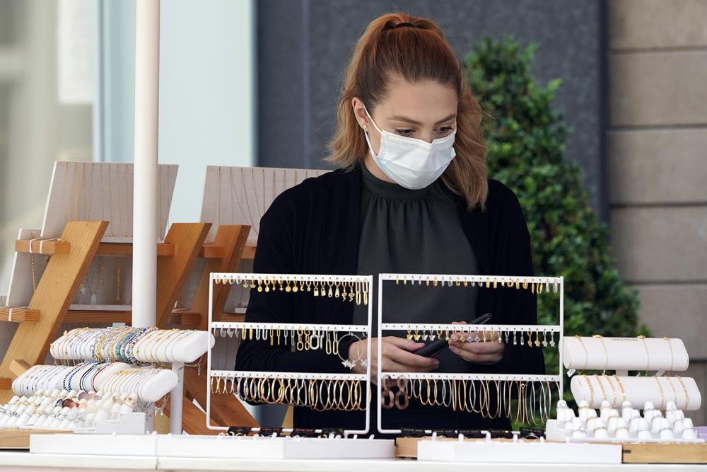 A worker wears a mask at an outdoor boutique amid the COVID-19 pandemic Thursday, May 20, 2021, at The Grove in Los Angeles. California regulators will shoot for a mid-June easing of workplace masking and social distancing requirements to conform with a broader state order. They asked to delay a debate Thursday on how quickly they should drop coronavirus safety rules for employees.