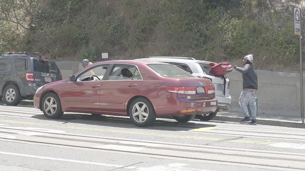 A suspected thief takes a suitcase out of the smashed back window of a parked SUV at Lombard and Hyde streets, June 15, 2021.