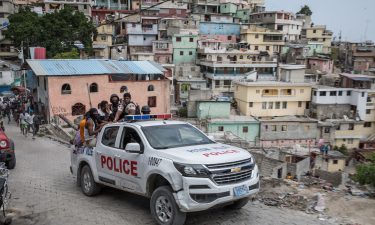 A police car filled with civilians and policemen drives up the Jalousie township where men accused of being involved in the assassination of President Jovenel Moise