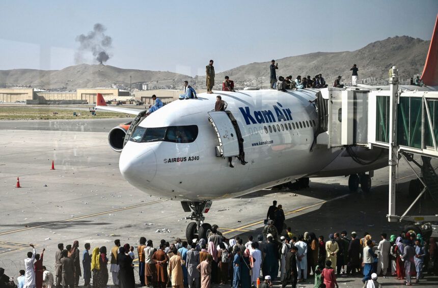 Afghan people climb atop a plane as they wait at the Kabul airport on Monday