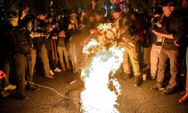 A Proud Boy adds fuel to a Black Lives Matter flag on fire as leader Enrique Tarrio and other members gather in the streets following the 'Million MAGA March' on December 12