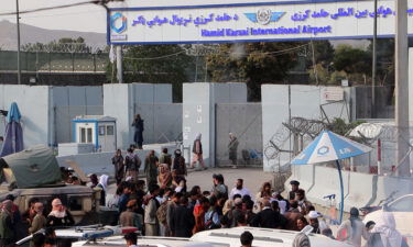 Taliban fighters stand guard as Afghans gather outside the Hamid Karzai International Airport to flee the country