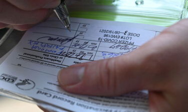 A nurse marks a coronavirus vaccination card with a third booster dose of Pfizer