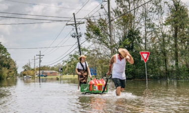 Residents move a cart with gas cans through a flooded neighborhood on Tuesday in Barataria