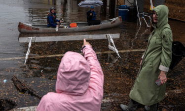 A woman points at two people paddling through flood water in a canoe in Old Town Alexandria