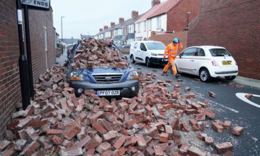 A man walks past a car lying under fallen masonry from a property Sunderland