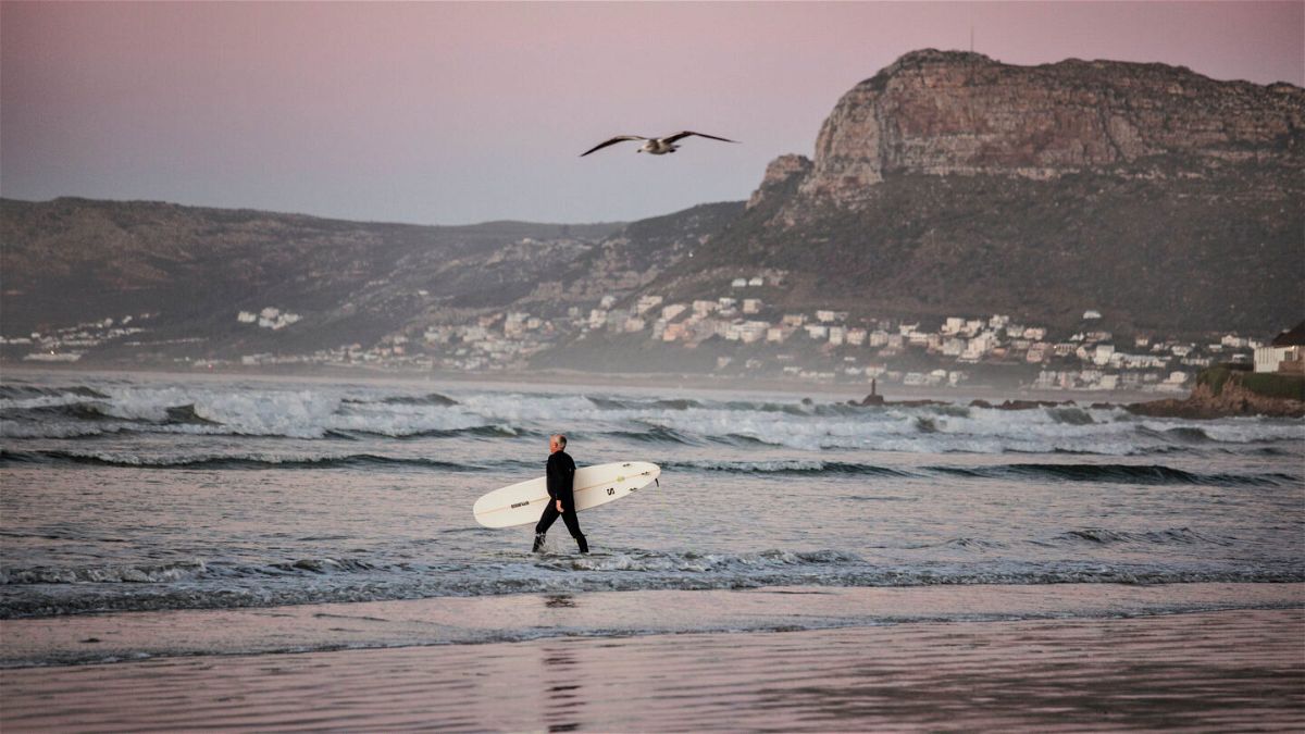<i>MARCO LONGARI/AFP via Getty Images</i><br/>A surfer carries his board as he braves the cold waters at sunrise in Muizenberg
