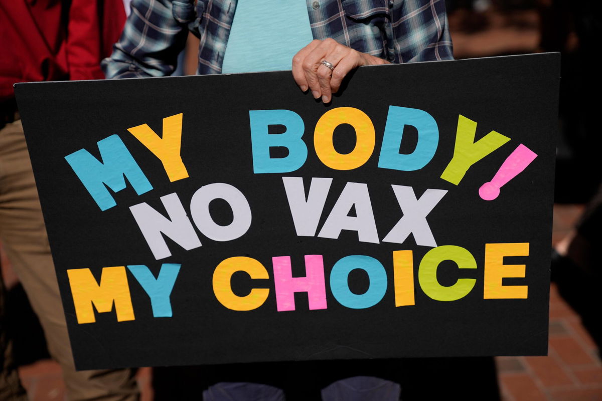 <i>Rebecca Blackwell/AP</i><br/>You can collect unemployment benefits in these states if you lose your job because of vaccine mandates. A person is seen holding a sign as several hundred anti-mandate demonstrators rally outside the Capitol on November 16