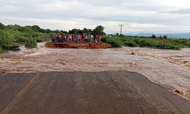 People stand on the other side of a road destroyed by tropical storm Ana