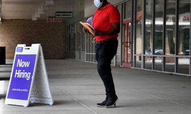 Pedestrians walk by a "Now Hiring" sign outside a store on August 16