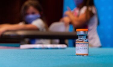 A vial of the new children's dose of the Pfizer-BioNTech Covid-19 vaccine sits in the foreground as children play in a hospital room waiting to be able to receive the vaccine at Hartford Hospital in Hartford