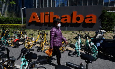 A woman walks past an Alibaba sign outside the company's office in Beijing on April 2021. Shares of Alibaba rose more than 11% on March 22 after the company announced it was boosting the size of its share buyback program.