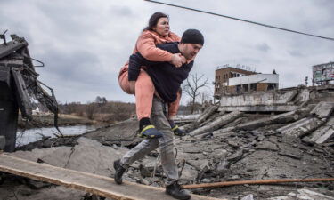 A man carries a woman as they cross an improvised path while fleeing Irpin