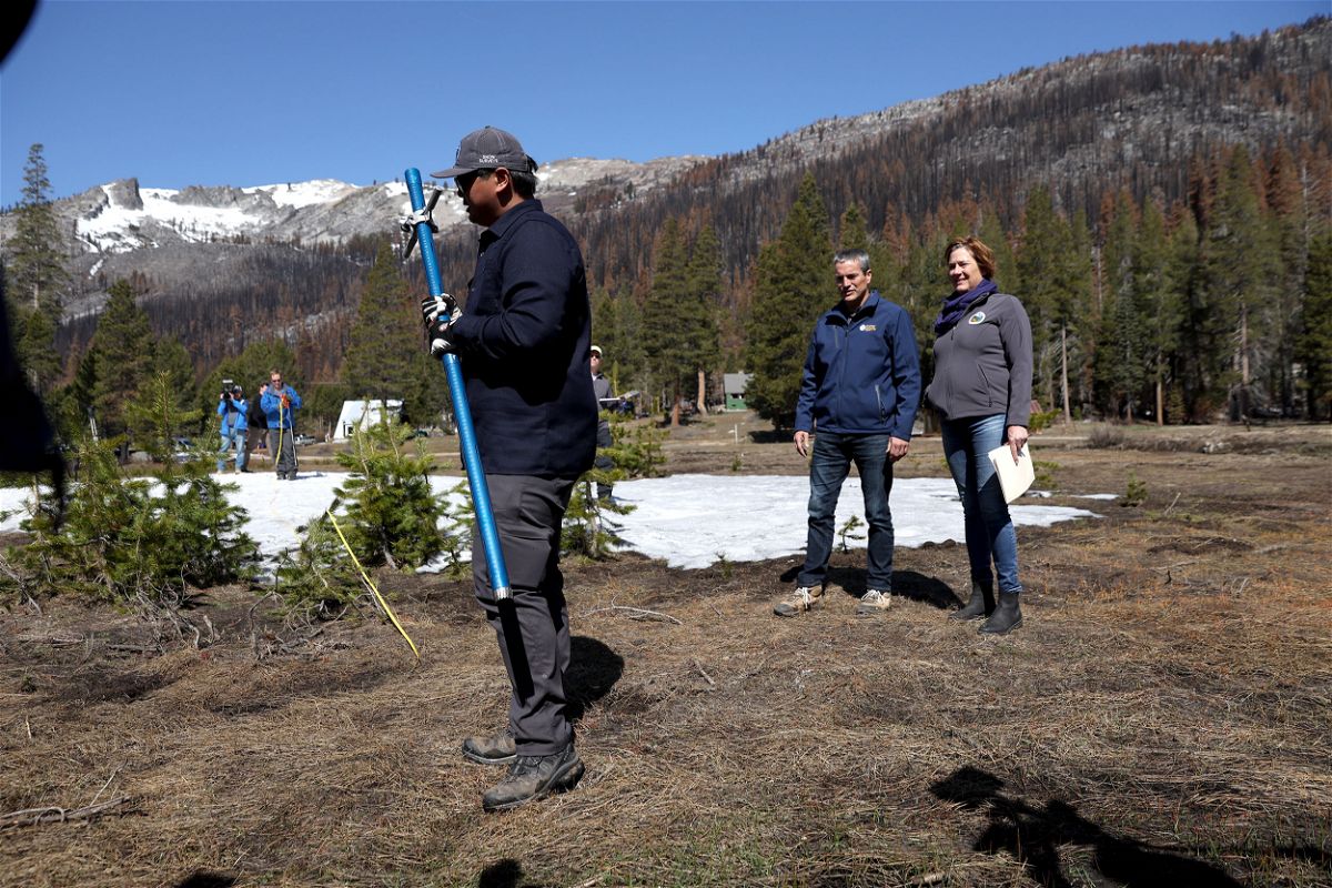 Sean de Guzman, manager of the California Department of Water Resources Snow Surveys Program, stands on dry ground with Director Karla Neme (right) and California Natural Resources Secretary Wade Crowfoot (center) while conducting the April 1 snowpack survey in Twin Bridges, California.