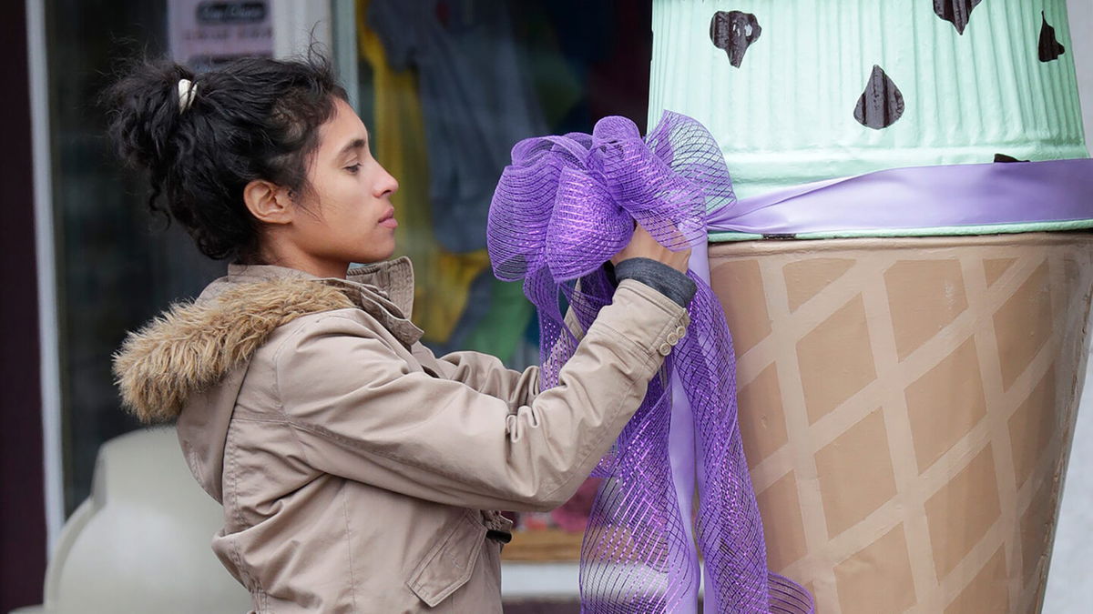 <i>Dan Powers/USA Today Network</i><br/>Ingrid Sievers ties a ribbon in front of an ice cream shop on April 26 as officials investigate the homicide.