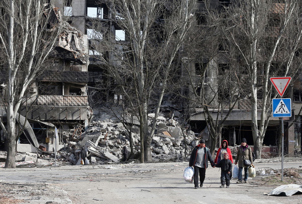 <i>Alexander Ermochenko/Reuters</i><br/>Local residents walk past an apartment building destroyed during the Ukraine-Russia conflict in Mariupol