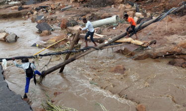 People walk across a makeshift bridge over a river