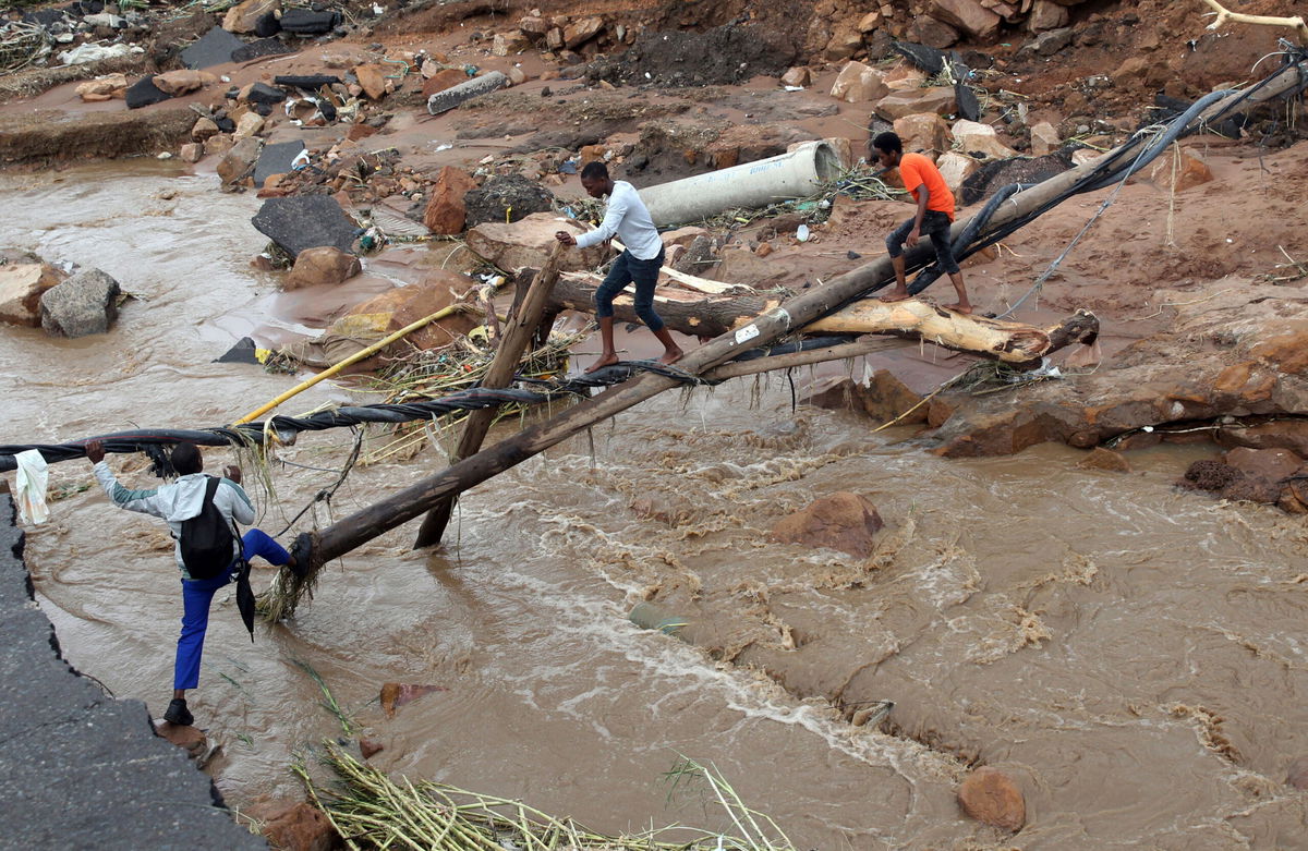 <i>AP</i><br/>People walk across a makeshift bridge over a river