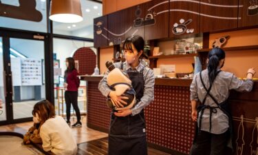 A worker holding a Lovot robot at a cafe in Kawasaki