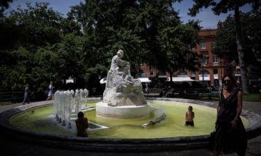 A pedestrian walks past as children play in a fountain in the city centre of Toulouse