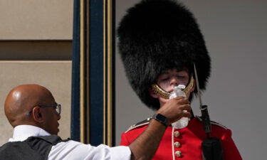 A police officer givers water to a British soldier wearing a traditional bearskin hat