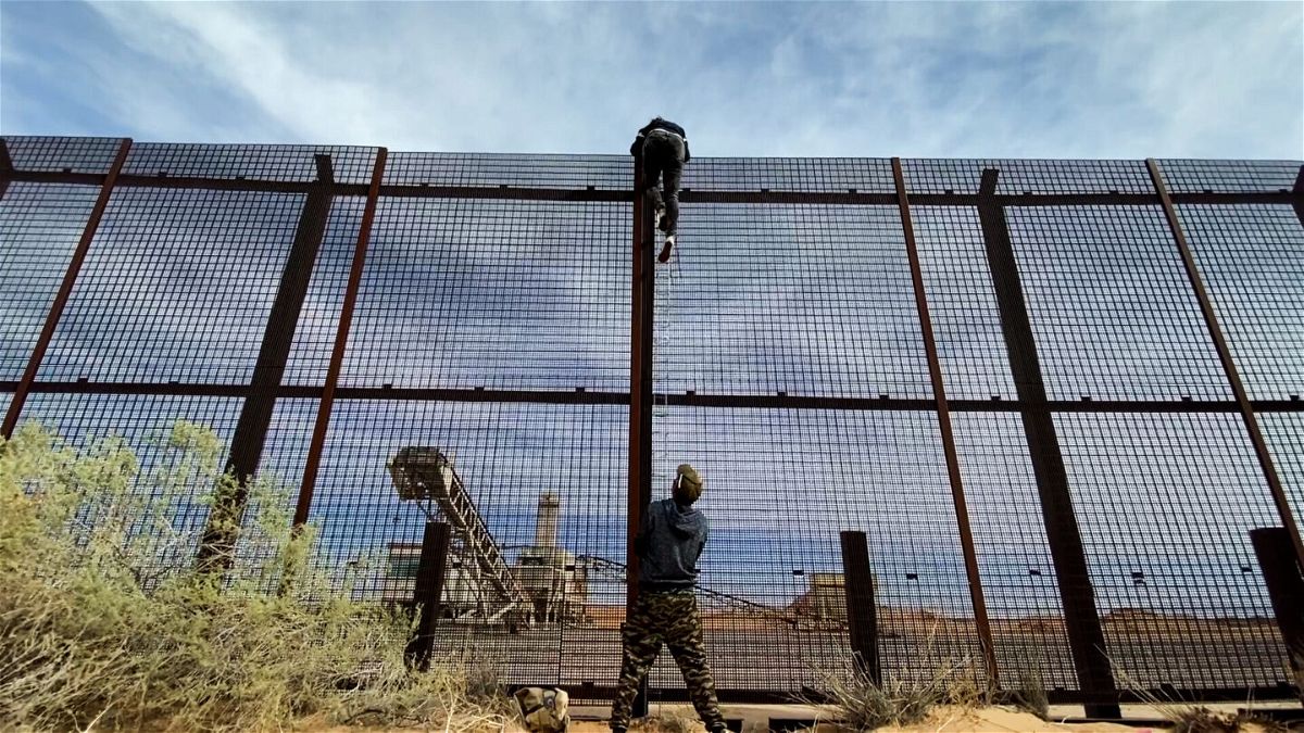 <i>Matt Rivers/CNN</i><br/>A 20 year-old female migrant from Ecuador is seen climbing over the US-Mexico border wall fence as the human smuggler that brought her to the wall steadies the ladder below.