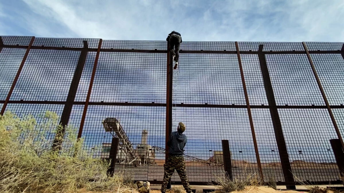 <i>Matt Rivers/CNN</i><br/>A 20 year-old female migrant from Ecuador is seen climbing over the US-Mexico border wall fence as the human smuggler that brought her to the wall steadies the ladder below.