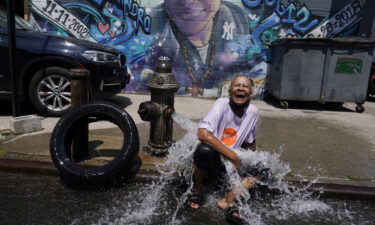 Sylvia Carrasquillo reacts as she sits in front of an open fire hydrant Friday in The Bronx neighborhood of New York City.