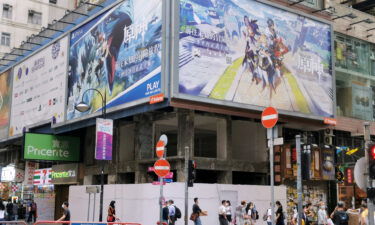 People walk below a billboard ad of fantasy game "Genshin Impact" in Hong Kong