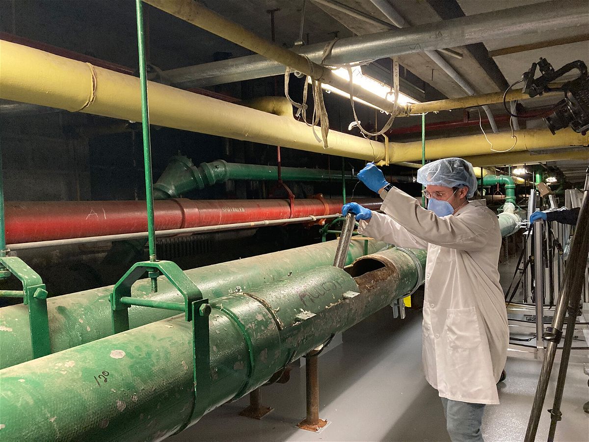 <i>NYC Health + Hospitals</i><br/>Queens College Research Assistant Justin Silbiger collects a wastewater sample from a sewage pipe in the basement of NYC Health + Hospitals/Elmhurst.