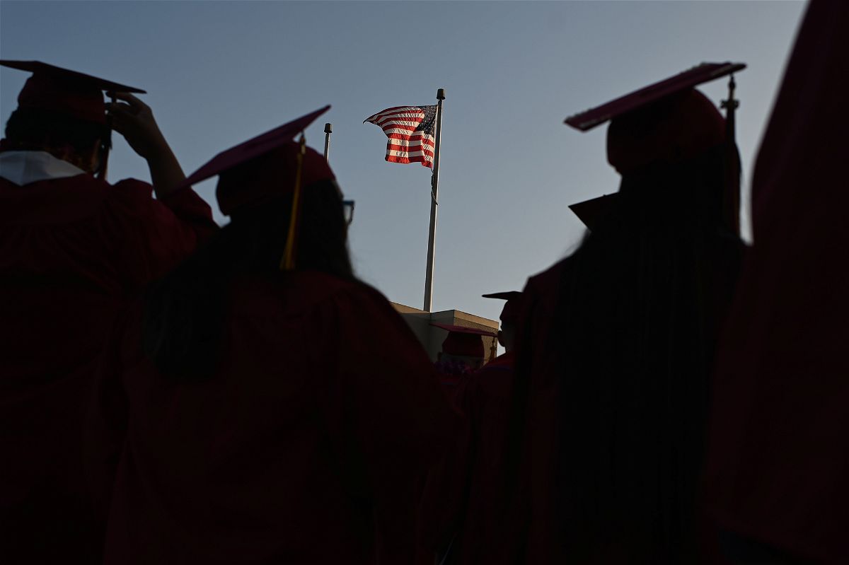 A US flag flies above a building as students earning degrees at Pasadena City College participate in the graduation ceremony, June 14, 2019, in Pasadena, California. - With 45 million borrowers owing $1.5 trillion, the student debt crisis in the United States has exploded in recent years and has become a key electoral issue in the run-up to the 2020 presidential elections.
