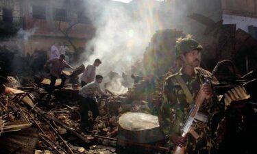 An Indian Muslim family looks for valuables from their burned home while an Indian army soldier stands guard in the downtown area of Ahmedabad