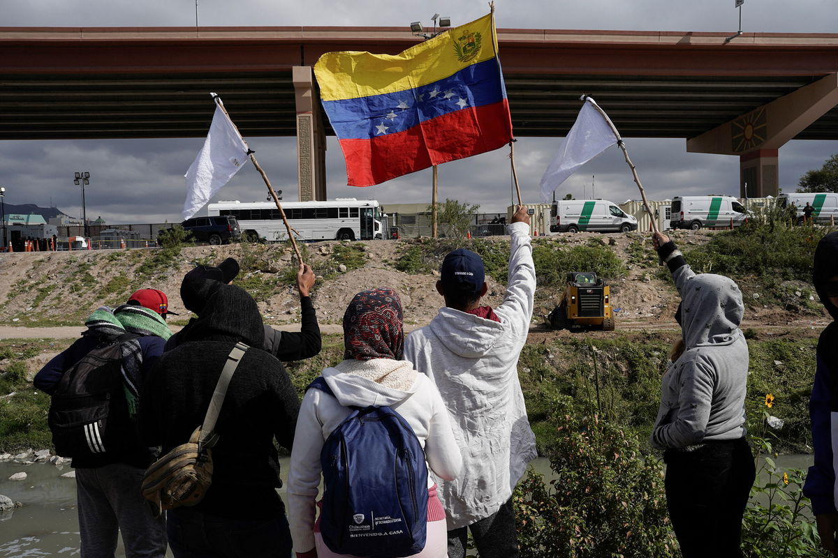 <i>Paul Ratje/Reuters</i><br/>Migrants wave flags on the banks of the Rio Grande Tuesday while peacefully protesting the new US migration enforcement rules.