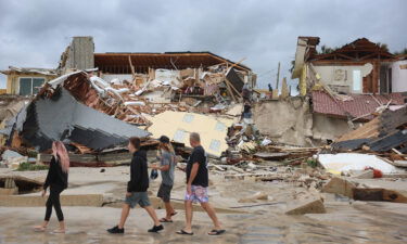 People look on at homes partially toppled onto the beach after Hurricane Nicole came ashore on November 10 in Daytona Beach