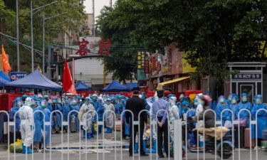 Law enforcers wearing white hazmat suits prepare to transfer residents in blue protective clothing at a high-risk neighborhood in Guangzhou on November 5.