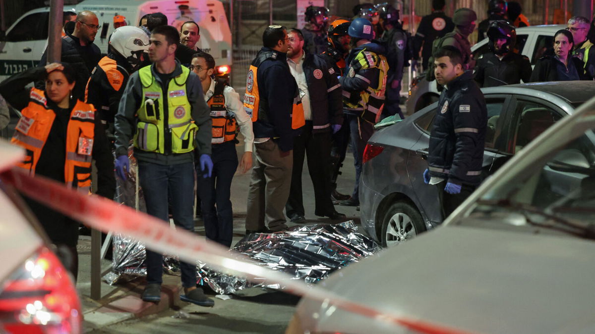 Israeli emergency service personnel and security forces stand near a covered body at the site of a reported attack in a settler neighbourhood of Israeli-annexed east Jerusalem, on January 27, 2023. (Photo by AHMAD GHARABLI / AFP) (Photo by AHMAD GHARABLI/AFP via Getty Images)