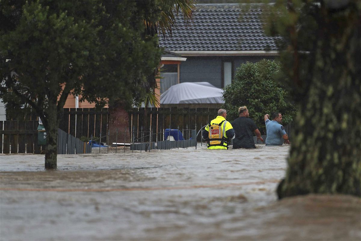 <i>Hayden Woodward/New Zealand Herald/AP</i><br/>Emergency workers and a man wade through flood waters in Auckland