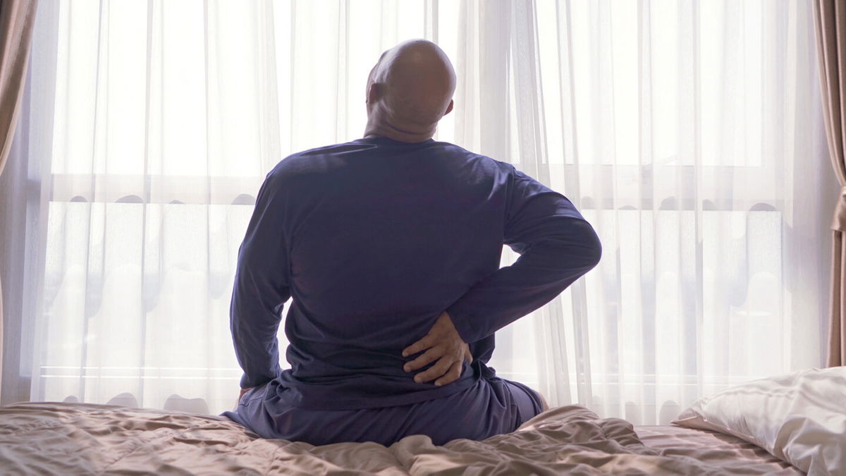 Old elderly black man. African American person waking up on bed in bedroom at home in early morning, suffering from backache or cramp. Back pain. Hurt muscle. Office syndrome.