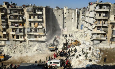 Syrian soldiers look on as rescuers use heavy machinery to sift through the rubble of a collapsed building in the northern city of Aleppo.