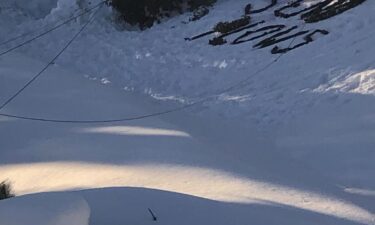 Krissy Marcum shared video with CNN that shows “SEND PLOWS” written out in black trash bags on top of a shady patch of snow as helicopters circle the area above.