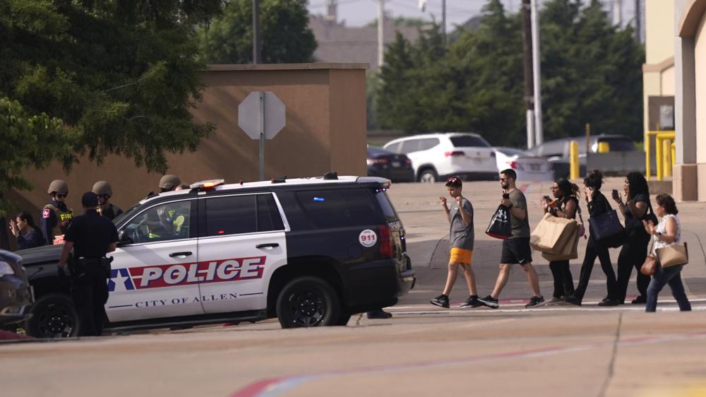 People raise their hands as they leave a shopping center after a shooting, Saturday, May 6, 2023, in Allen, Texas.