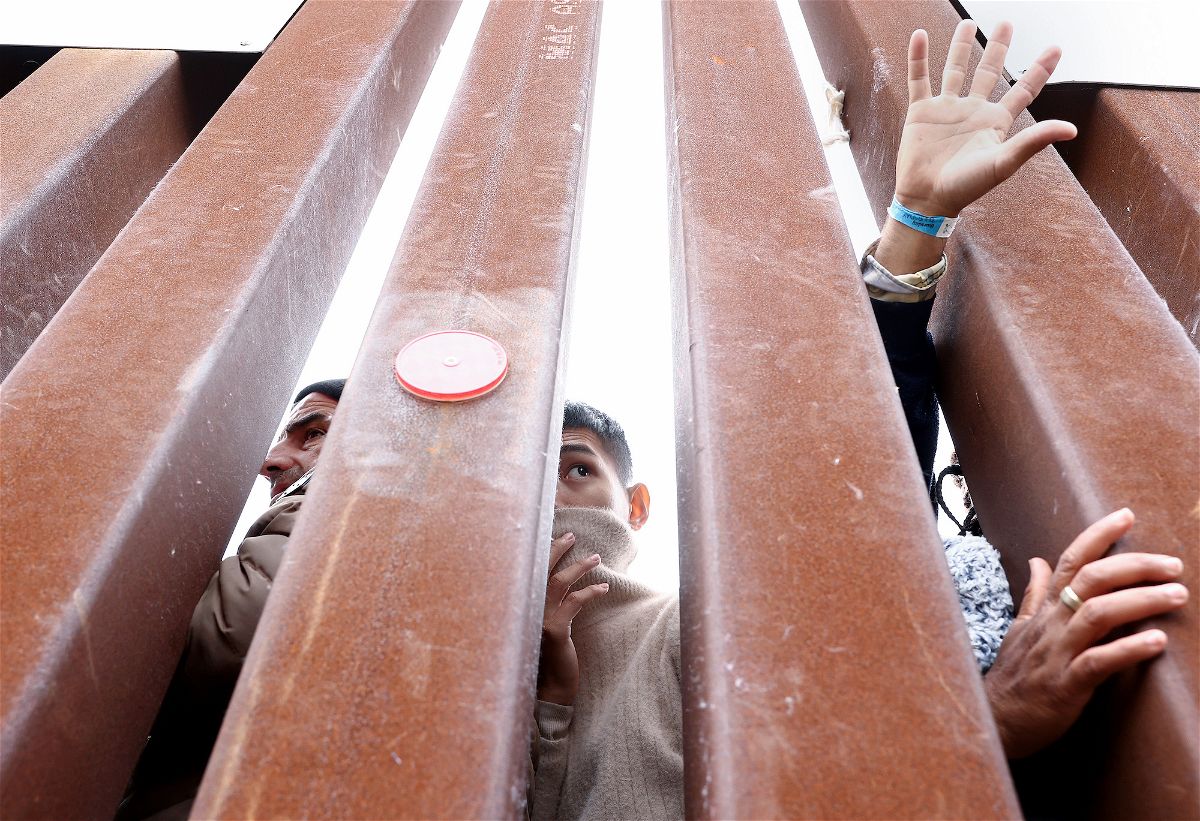 <i>Mario Tama/Getty Images</i><br/>Migrants seeking asylum in the US look through the border wall as volunteers offer assistance on the other side on May 13 in San Diego.