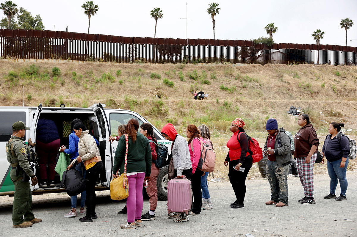 SAN DIEGO, CALIFORNIA - MAY 13: A U.S. Border Patrol agent keeps watch as immigrants enter a vehicle to be transported from a makeshift camp between border walls, between the U.S. and Mexico, on May 13, 2023 in San Diego, California. Some of the immigrants at the open air camp have been waiting for days in limbo for a chance to plead for asylum while local volunteer groups are providing food and other necessities. The U.S. government's Covid-era Title 42 policy, which for the past three years had allowed for the quick expulsion of irregular migrants entering the country, expired on the evening of May 11. (Photo by Mario Tama/Getty Images)