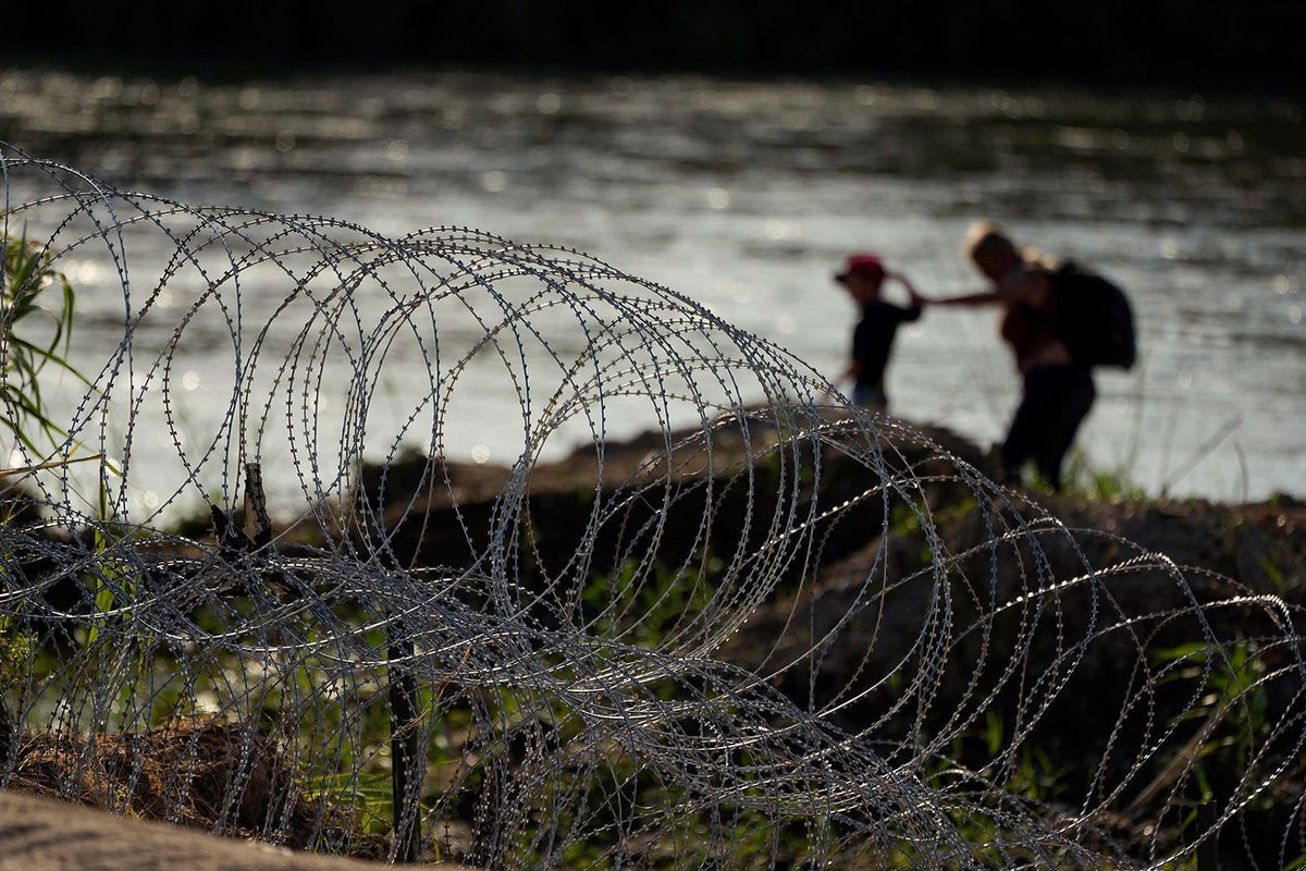 <i>Eric Gay/AP/FILE</i><br/>Migrants walk along concertina wire as they try to cross the Rio Grande in Eagle Pass