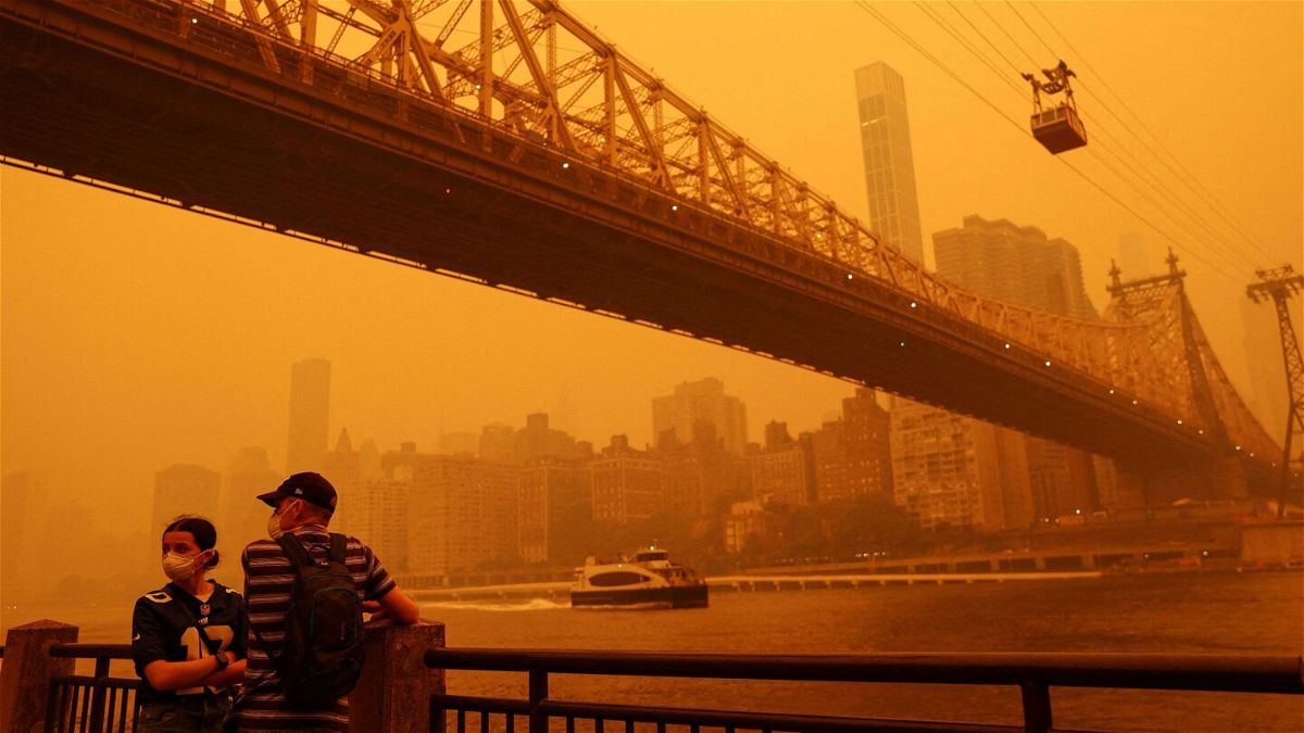 <i>Shannon Stapleton/Reuters/FILE</i><br/>People wear protective masks as the Roosevelt Island Tram crosses the East River while haze and smoke from the Canadian wildfires shroud the Manhattan skyline in the Queens Borough New York City