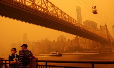 People wear protective masks as the Roosevelt Island Tram crosses the East River while haze and smoke from the Canadian wildfires shroud the Manhattan skyline in the Queens Borough New York City