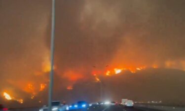 Firefighters protectively spray water on homes as forest fires burn nearby.