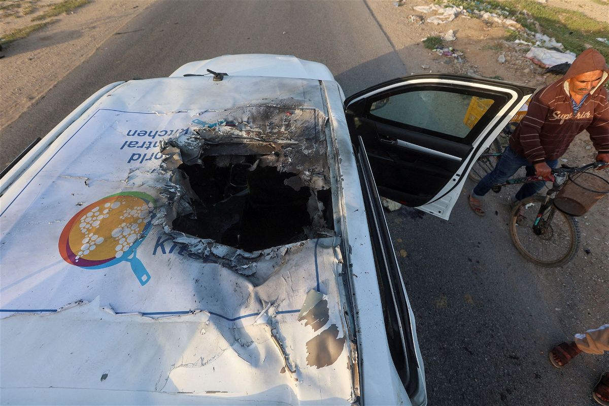 A Palestinian man rides a bicycle past a damaged vehicle where employees from the World Central Kitchen were killed in an Israeli airstrike, according to the NGO.