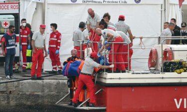 Rescuers carry a body after divers return in Porticello harbor in Sicily